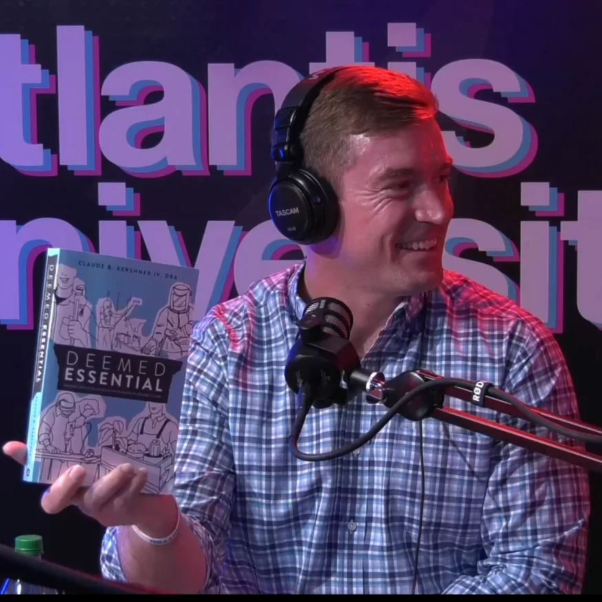 Dr. Claude Kershner IV holding a copy of Deemed Essential in a podcast studio