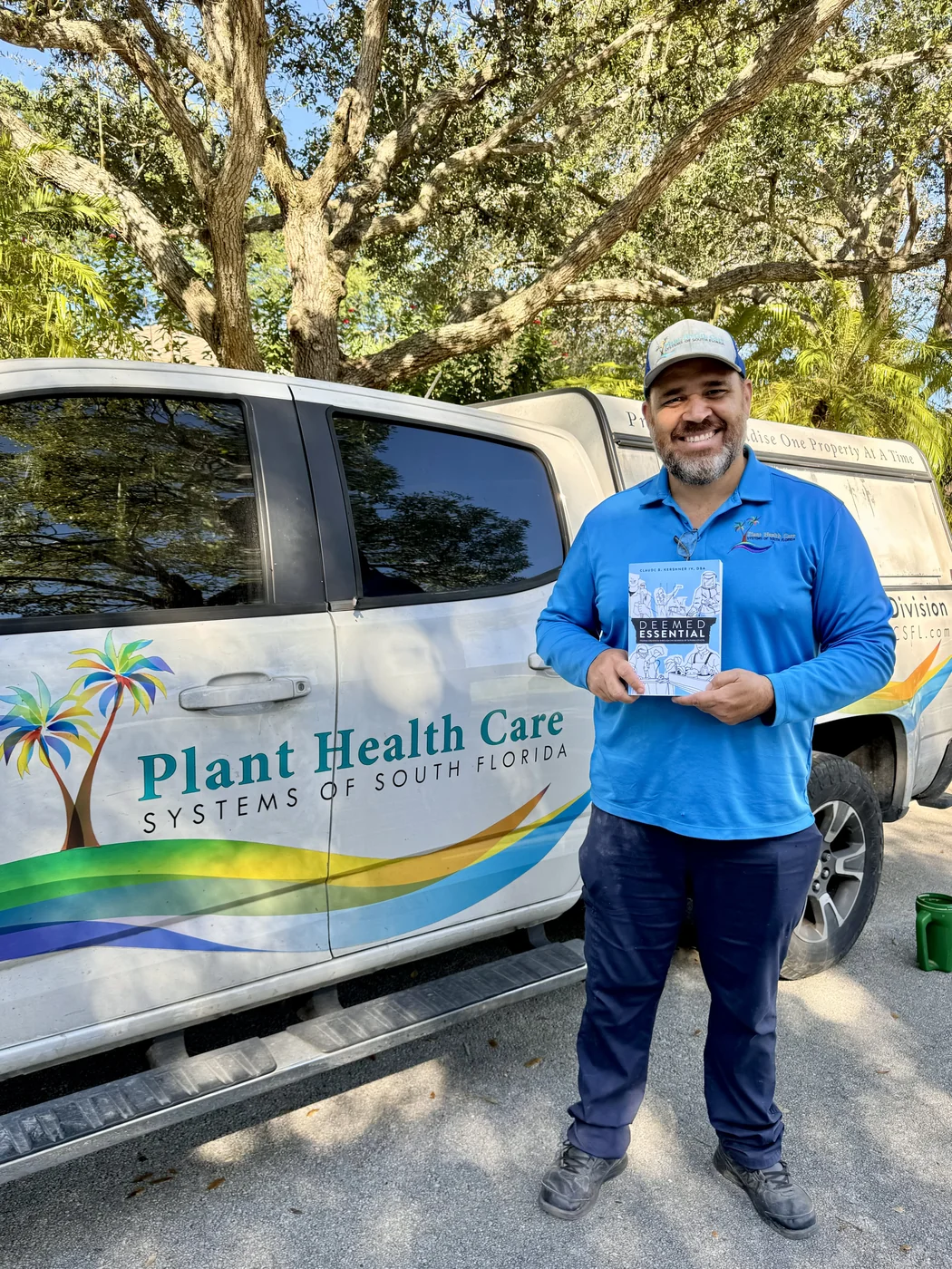 A field-service professional holding a copy of Deemed Essential beside a company vehicle
