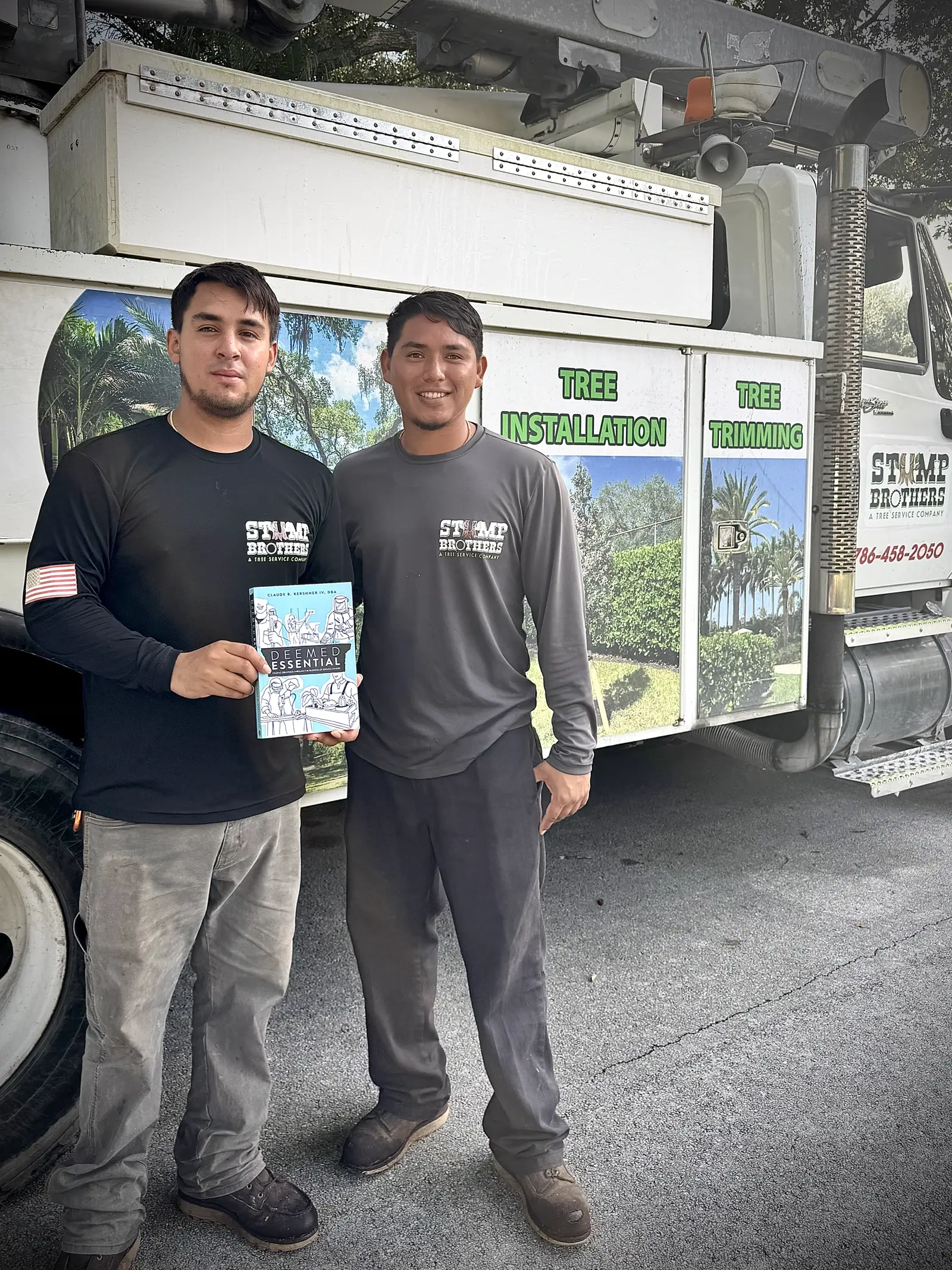 Two tree-service professionals holding Deemed Essential beside their work truck