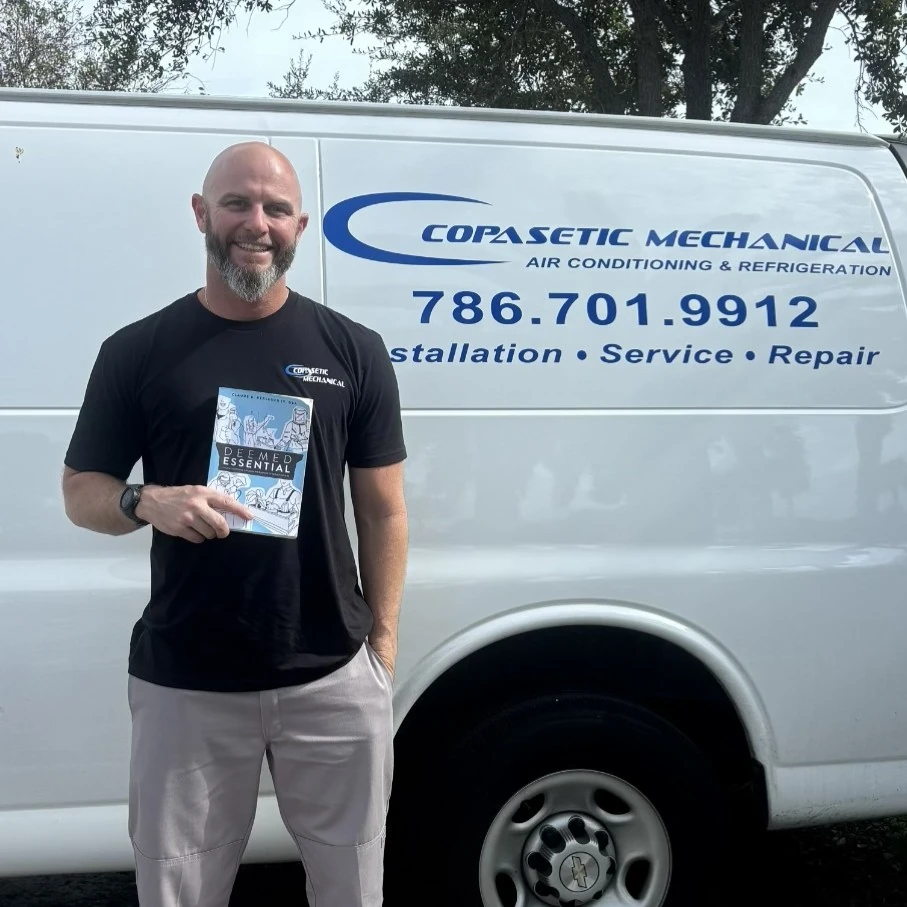 Ryan Connolly holding a copy of Deemed Essential beside a service van